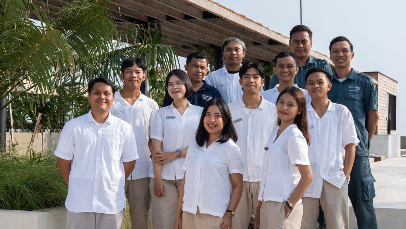 Eleven members of the Body Factory Lifestyle Residence Uluwatu staff team in white uniform shirts and beige trousers stand together on an open-air rooftop terrace